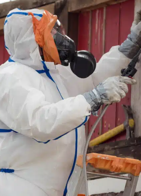 Opérateur en combinaison de protection et masque respiratoire utilisant un pulvérisateur pour le traitement ou l'encapsulation de l'amiante.