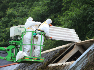 Deux ouvriers certifiés en protection individuelle effectuant le retrait d'une toiture en amiante à l'aide d'une nacelle.