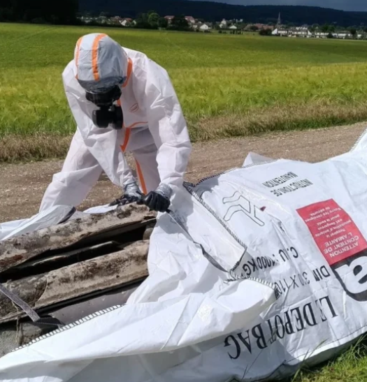Ouvrier en équipement de protection manipulant et emballant des déchets d'amiante dans un sac de confinement sécurisé.